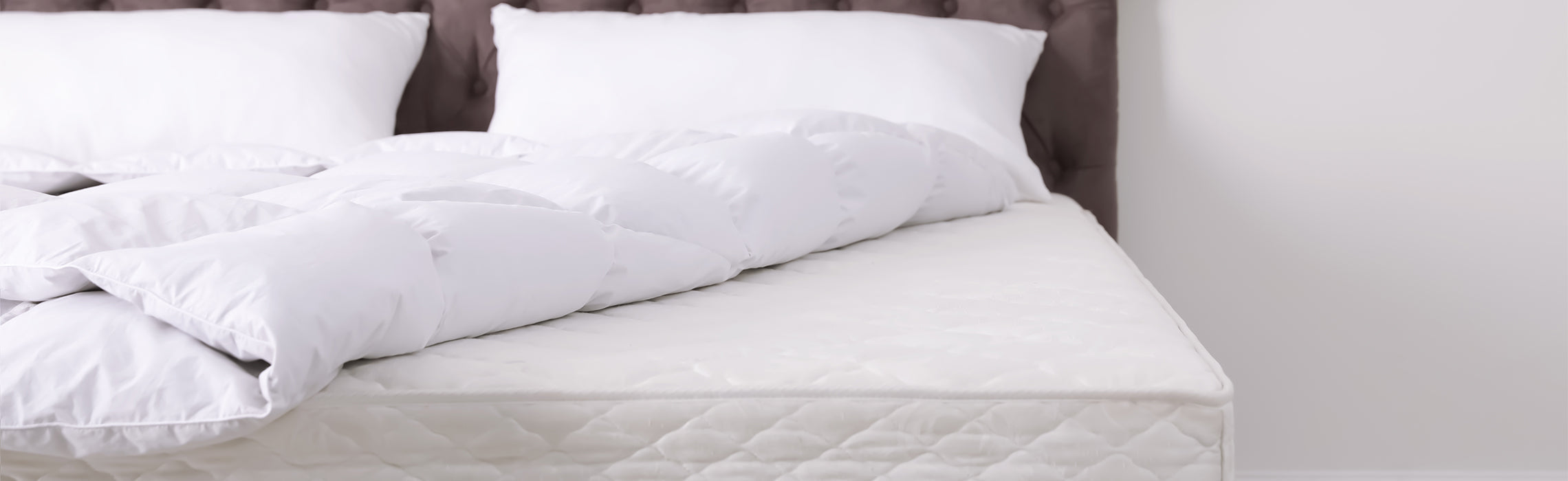White mattress with a quilted pattern and a long body pillow across neatly arranged white pillows against a tufted headboard, representing sleep comfort, bedding support, and a clean modern bedroom.