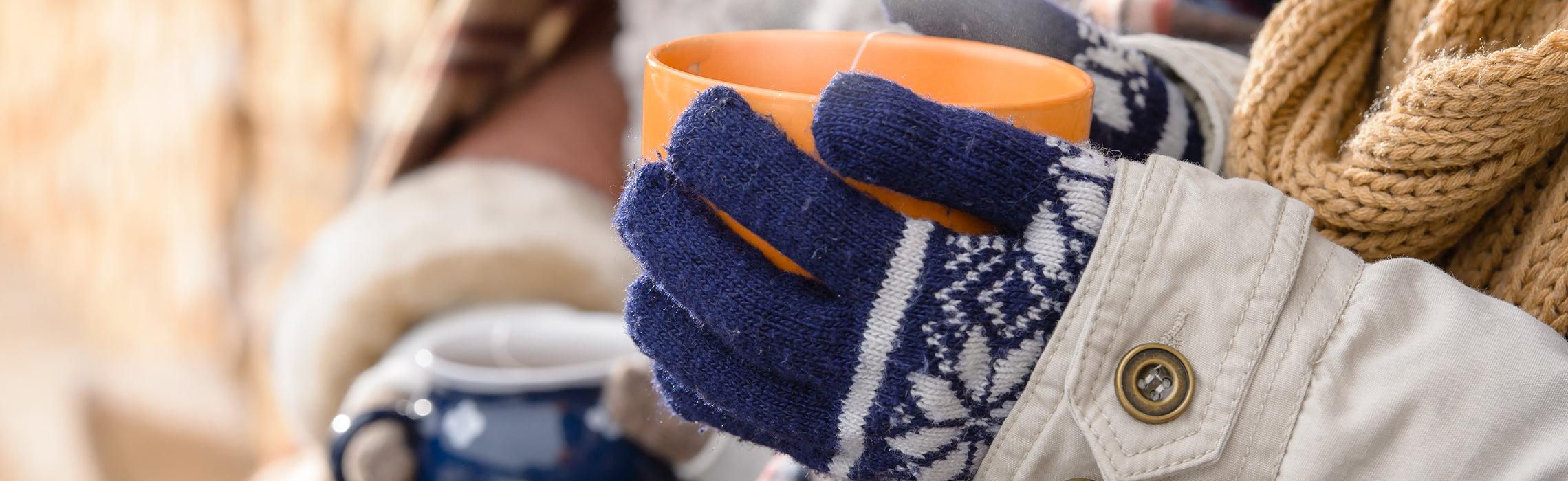 Person wearing winter gloves and a scarf holds a warm mug outdoors in cold weather.