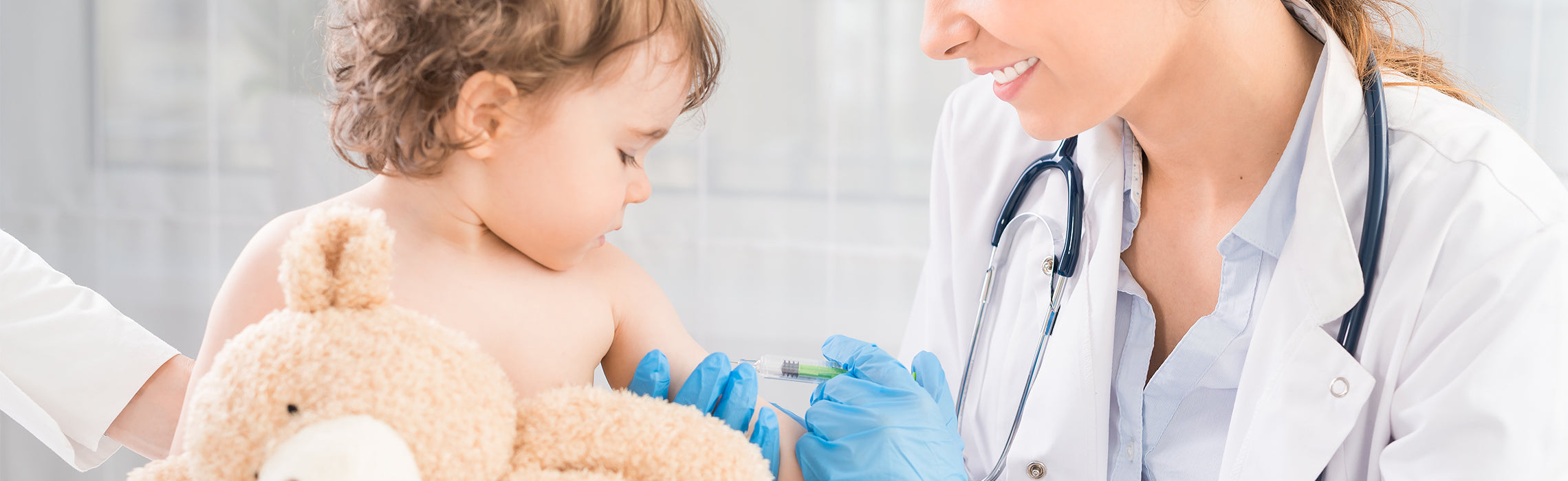 Healthcare provider wearing a lab coat and gloves administering a vaccine injection to a young child holding a teddy bear, representing pediatric care, immunization, and preventive healthcare.