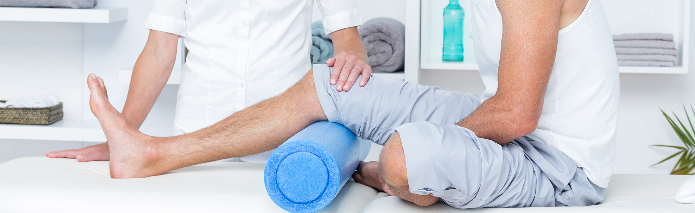Healthcare professional assisting a patient performing leg therapy with a blue foam roller on a treatment table, representing physical therapy, knee rehabilitation, and muscle recovery.