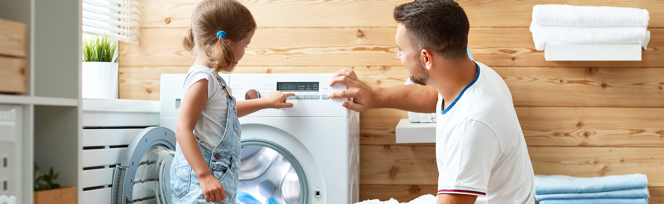 Person and child operating a front-load washing machine together in a bright laundry room, demonstrating safe home appliance use and family household activity.