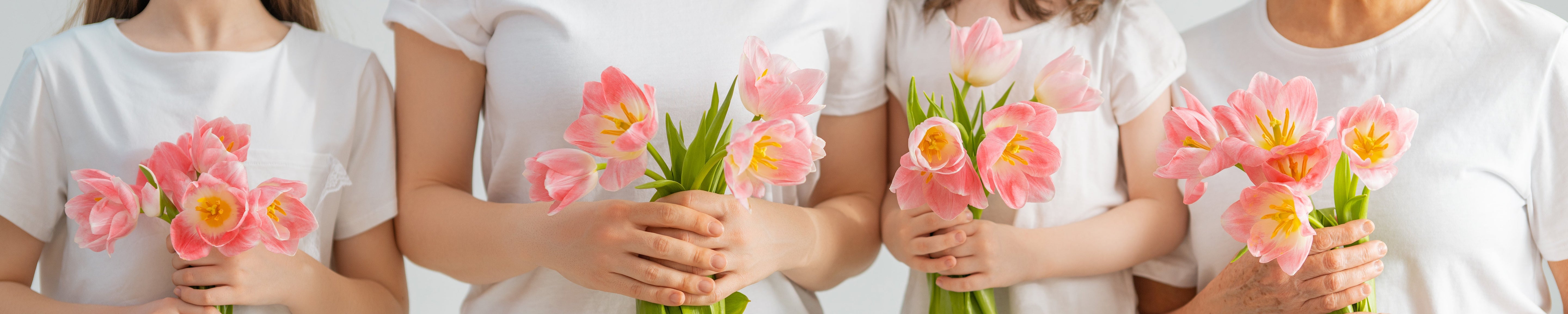 Four people in white tops each hold a small bouquet of pink flowers against a soft, neutral background, emphasizing spring, care, and togetherness. No visible text or branding.