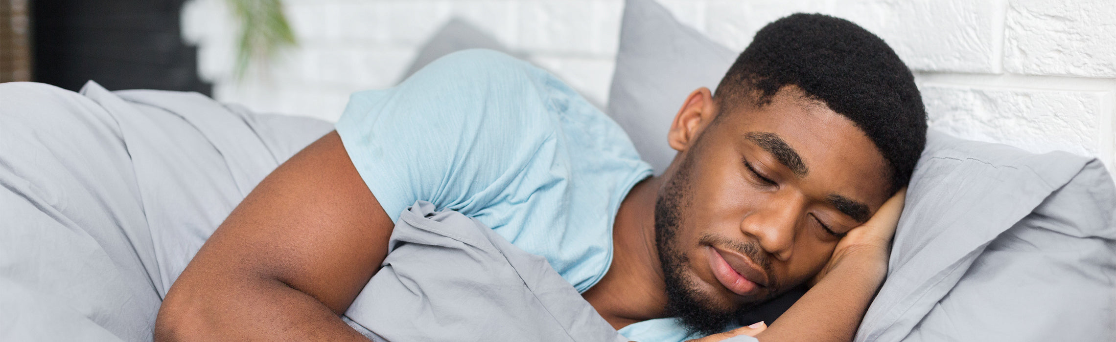 Person lying on a bed in a side sleeping position with head on a pillow and covered by gray bedding, representing restful sleep, comfort, and healthy sleep habits.