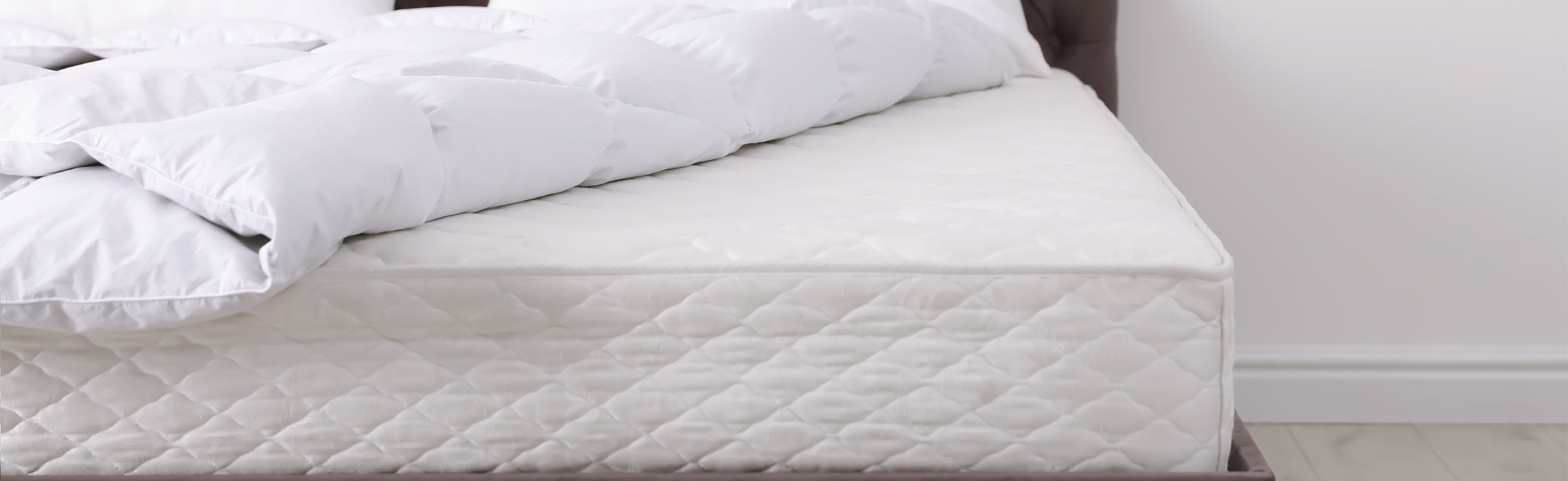White quilted mattress with folded pillow-top bedding neatly placed on top in a clean bedroom setting, representing sleep comfort, mattress support, and home bedding essentials.