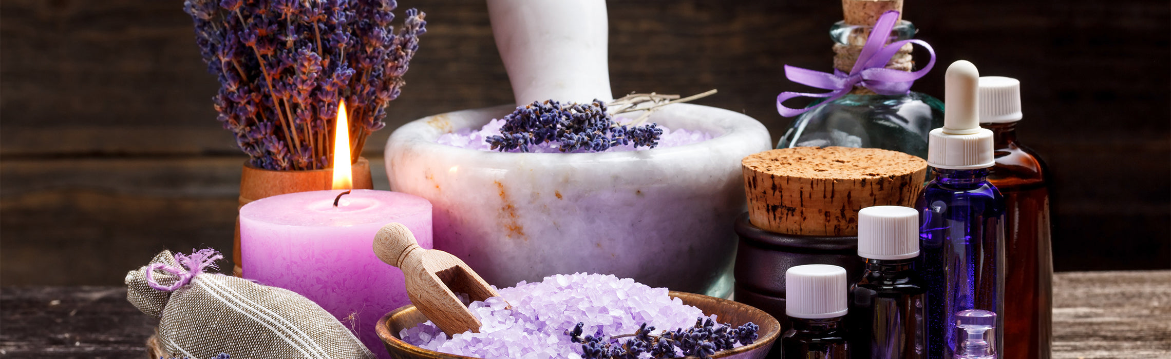 Lavender spa setup with a lit candle, essential oil bottles, bath salts, and dried lavender on a wooden surface, representing relaxation, aromatherapy, and wellness.