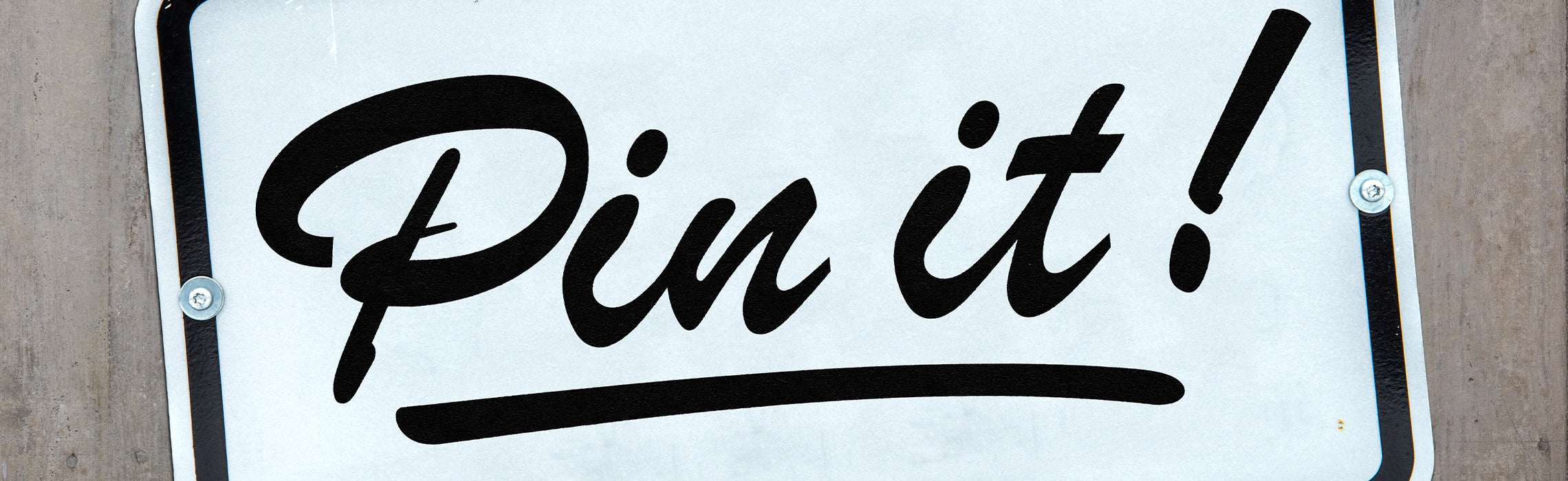 Close-up of a white sign with bold black script text reading “Pin it!” with an underline, mounted on a wall, representing social media sharing, Pinterest content, and digital engagement.