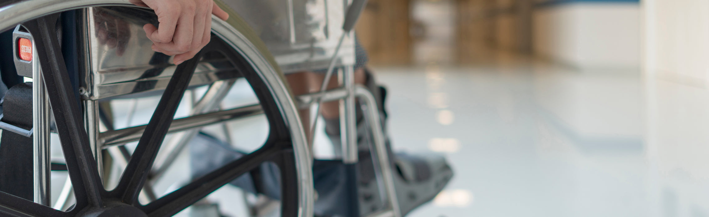 Close-up of a person seated in a wheelchair with hand resting on the wheel rim in a bright indoor space, representing mobility, accessibility, and independent living.