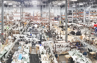 Large warehouse with rows of sewing machines, organized workstations, and workers producing goods, representing industrial manufacturing and mass production.