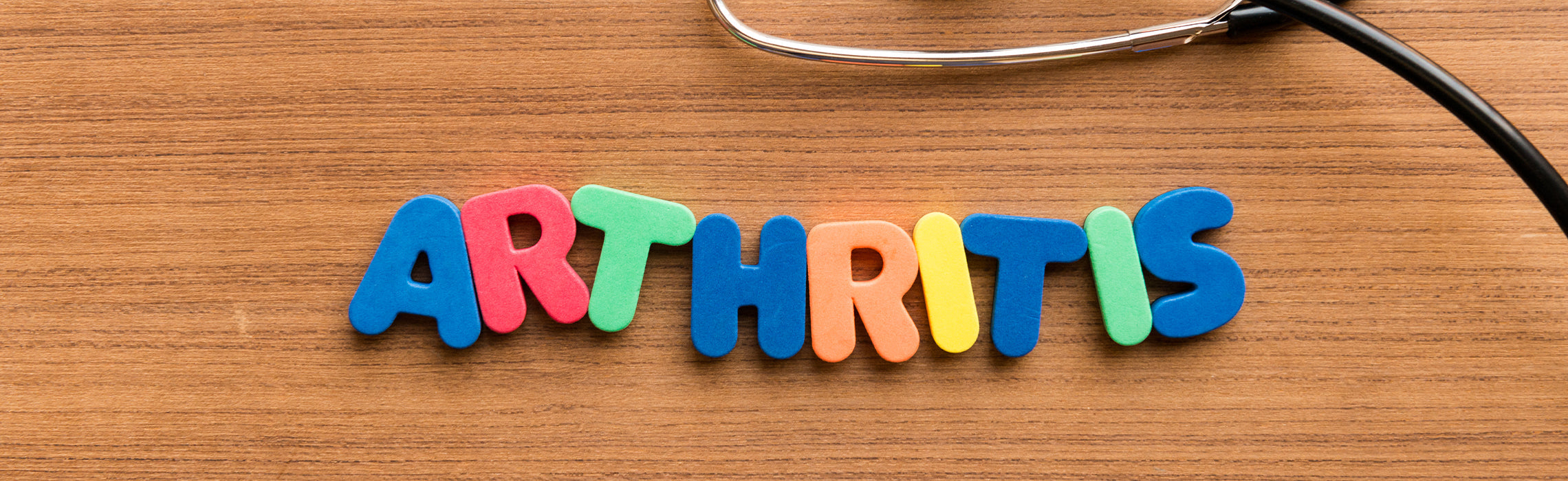 Colorful letter blocks spelling “ARTHRITIS” on a wooden surface beside a stethoscope.