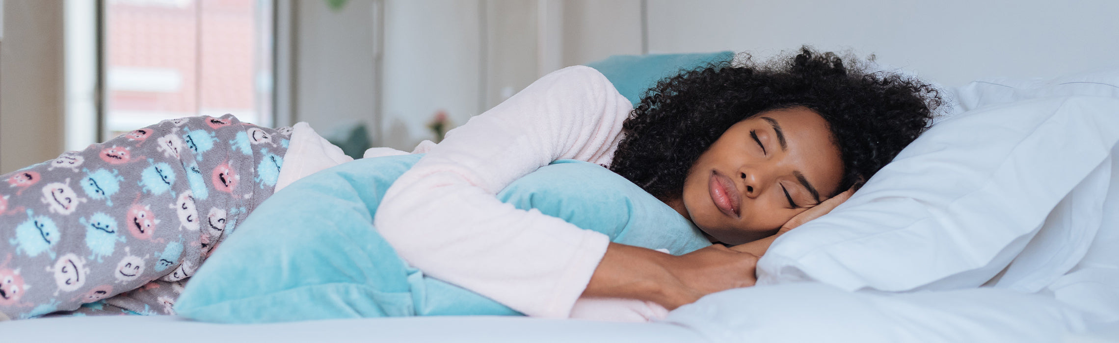 Person lying on a bed in a side sleeping position, hugging a supportive blue body pillow with head resting on a white pillow, representing comfortable sleep, proper alignment, and bedtime relaxation.