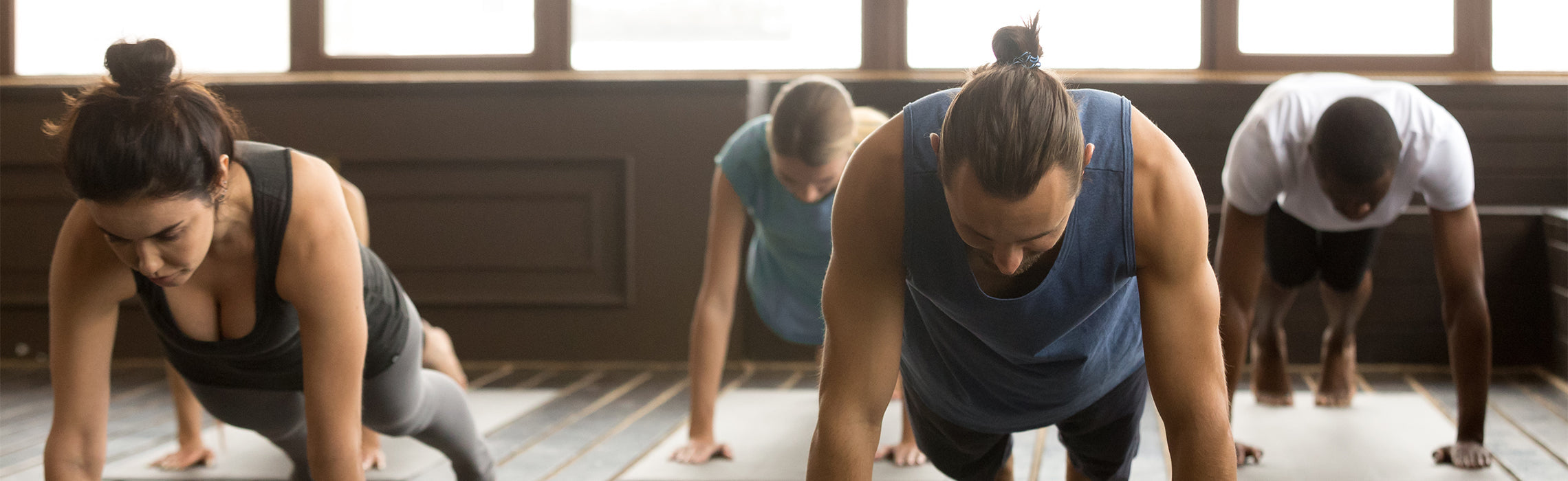 Group of people in a fitness studio holding plank position on yoga mats, representing group exercise, strength training, core workouts, and indoor fitness classes.