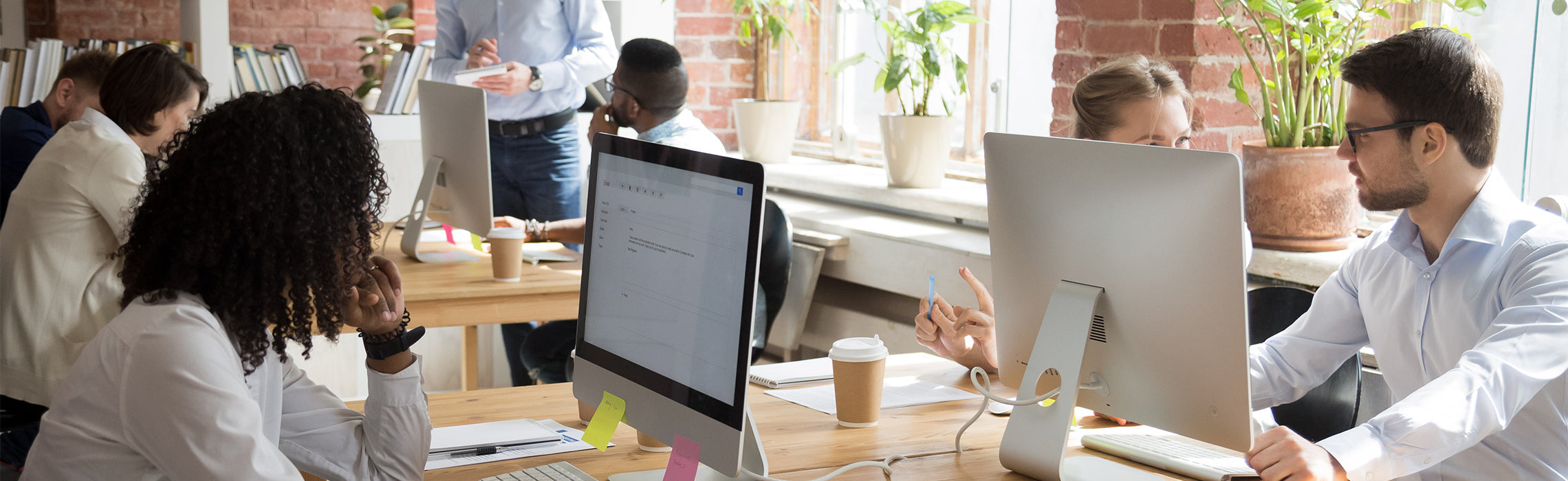 Modern office workspace with employees collaborating at desktop computers in a bright open-concept environment.
