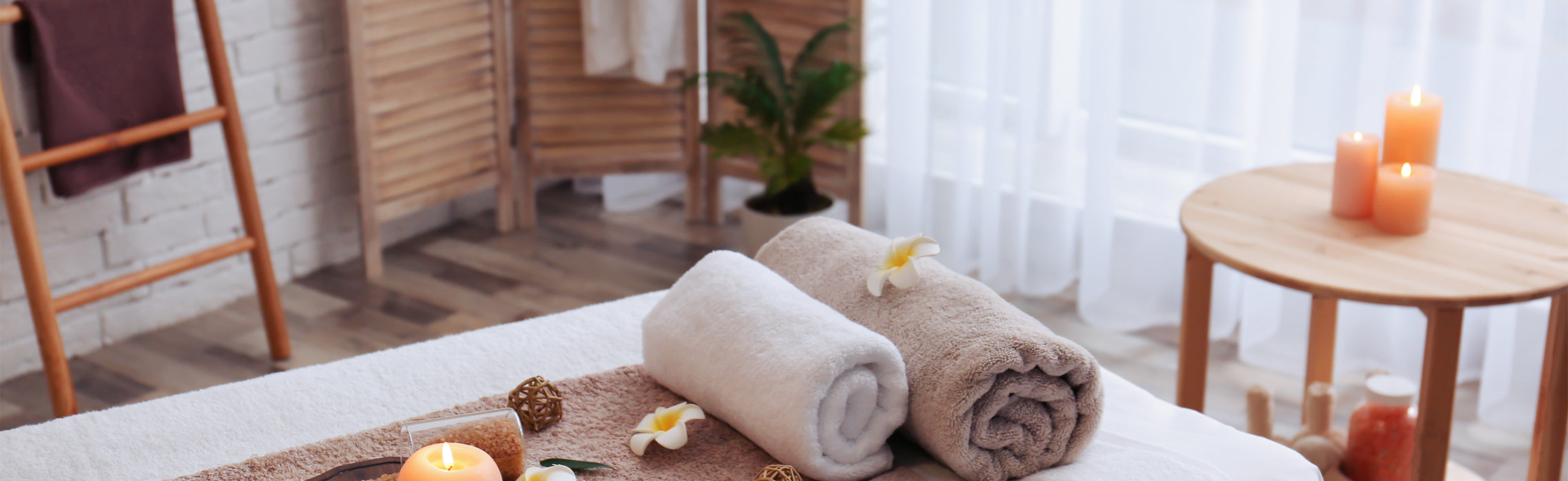 Rolled white and beige towels with candles and spa decor on a massage table in a calm wellness setting, representing relaxation, self-care, and spa treatment.