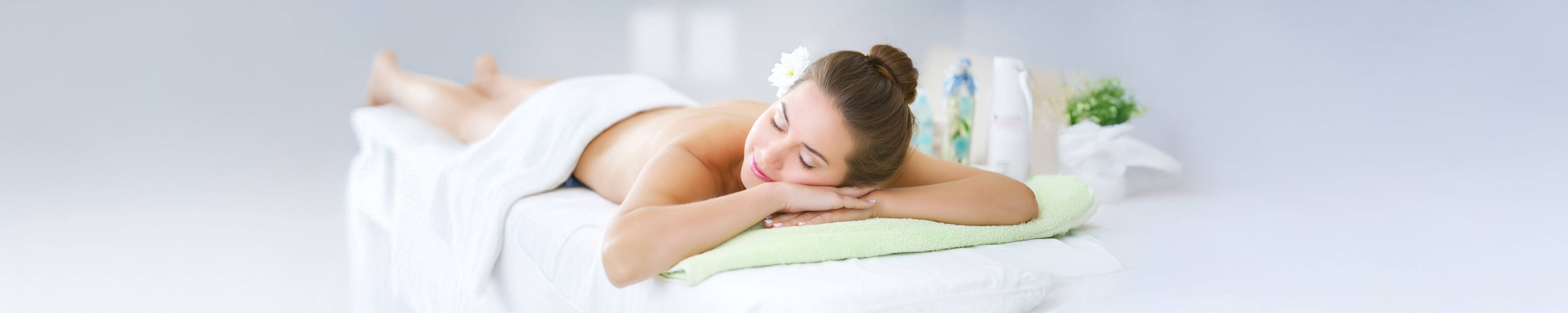 Person lying face down on a spa treatment table with a towel and head resting on folded arms, surrounded by soft lighting and wellness decor, representing massage therapy, relaxation, and self-care.