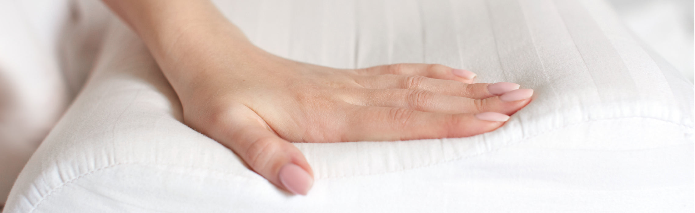 Close-up of a hand pressing into a white pillow, showing its softness and support, representing bedding comfort, pressure relief, and product quality.