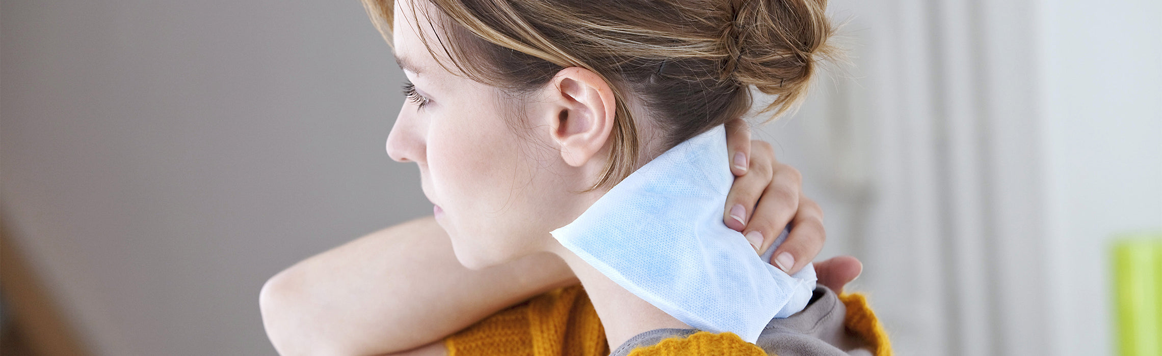 Person holding a cold pack against the back of the neck indoors, wearing a sweater, representing neck pain relief, muscle strain treatment, and at‑home therapy.