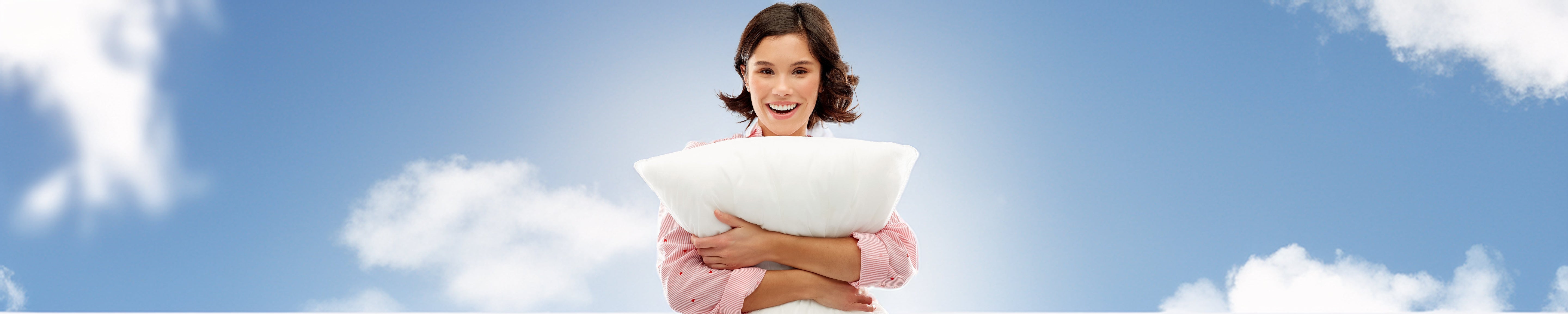 Person holding a white pillow against a blue sky with soft clouds, highlighting comfort, sleep quality, and relaxation; bright, airy setting. No visible text.