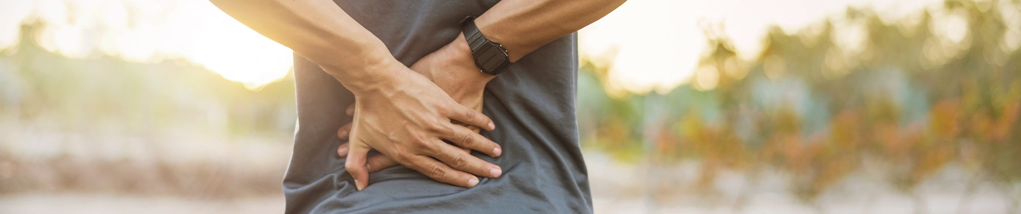 Back pain relief lifestyle banner featuring a person holding their lower back outdoors; no visible text, highlighting discomfort, support needs, and pain relief solutions for active living.