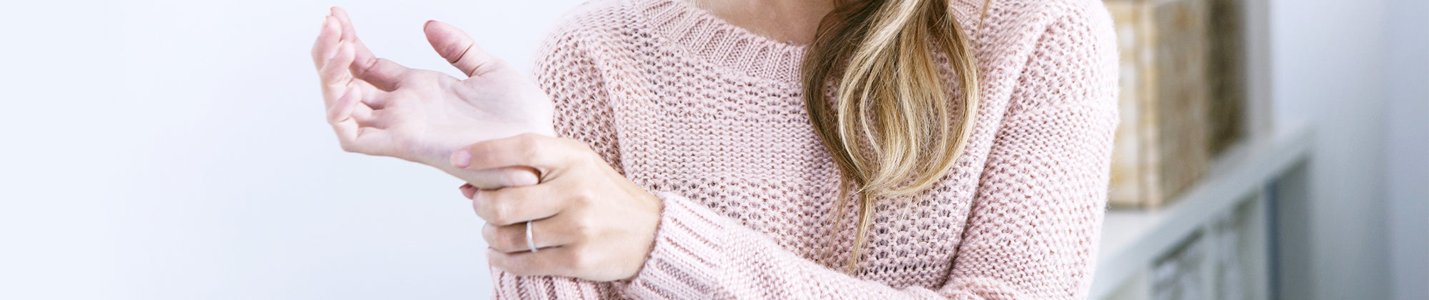 Core Products arthritis pain relief lifestyle banner featuring a woman in a sweater holding her wrist; no visible text, highlighting joint discomfort, hand support, and soothing relief solutions.
