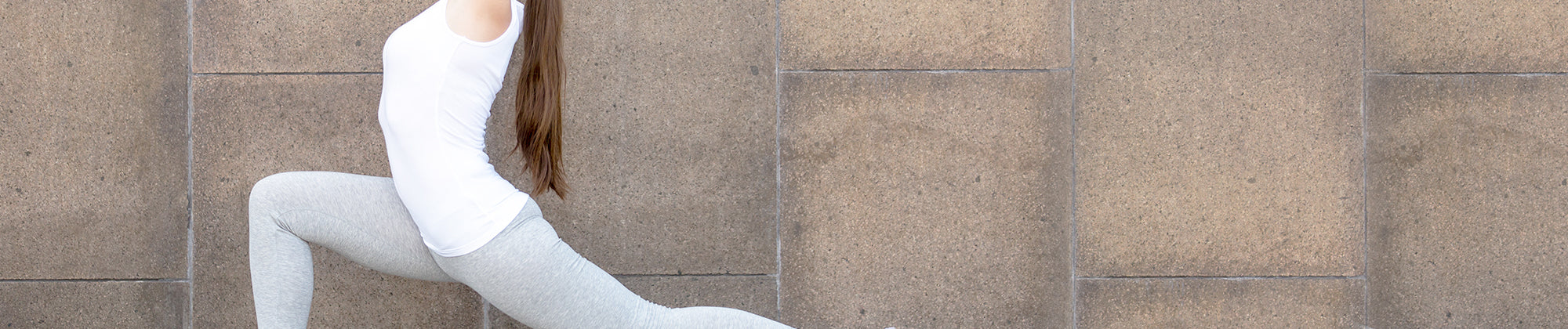 wellness lifestyle banner featuring a woman in white activewear performing a stretch against a neutral tiled wall; no visible text, highlighting flexibility, movement, and overall body wellness.