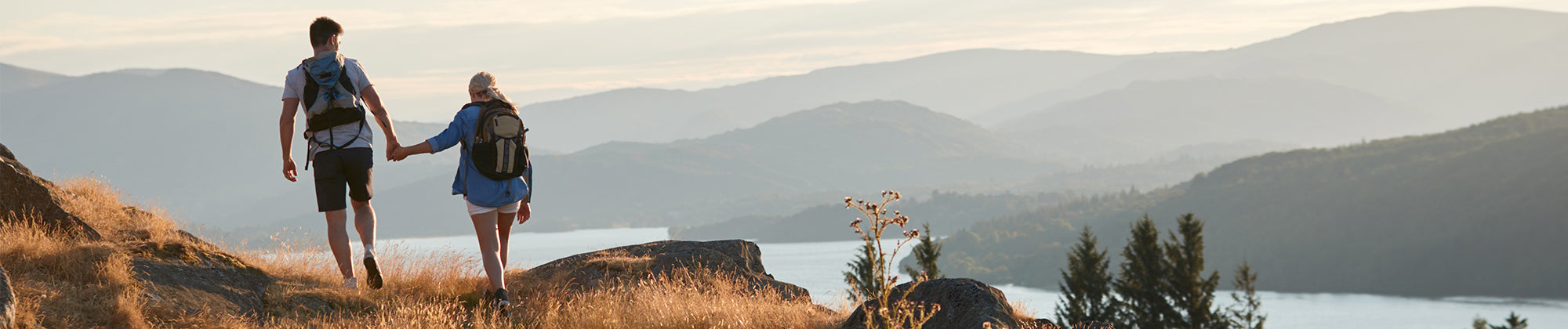 active lifestyle banner featuring a couple hiking on a scenic mountain trail overlooking water; no visible text, highlighting mobility, endurance, and outdoor wellness.