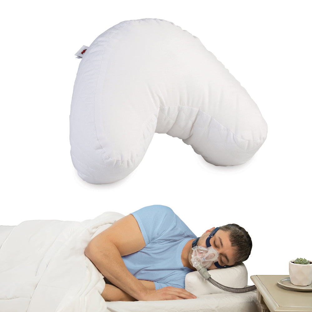 Core Products® Mini CPAP Pillow featuring a white, compact contoured design with a curved shoulder cutout and quilted side panels. The image shows the pillow above a man sleeping on his side while wearing a CPAP mask, with the hose extending over the pillow's edge. The specially shaped pillow helps accommodate CPAP masks and tubing, reduce pressure points, and provide comfortable support for side sleeping during CPAP therapy.