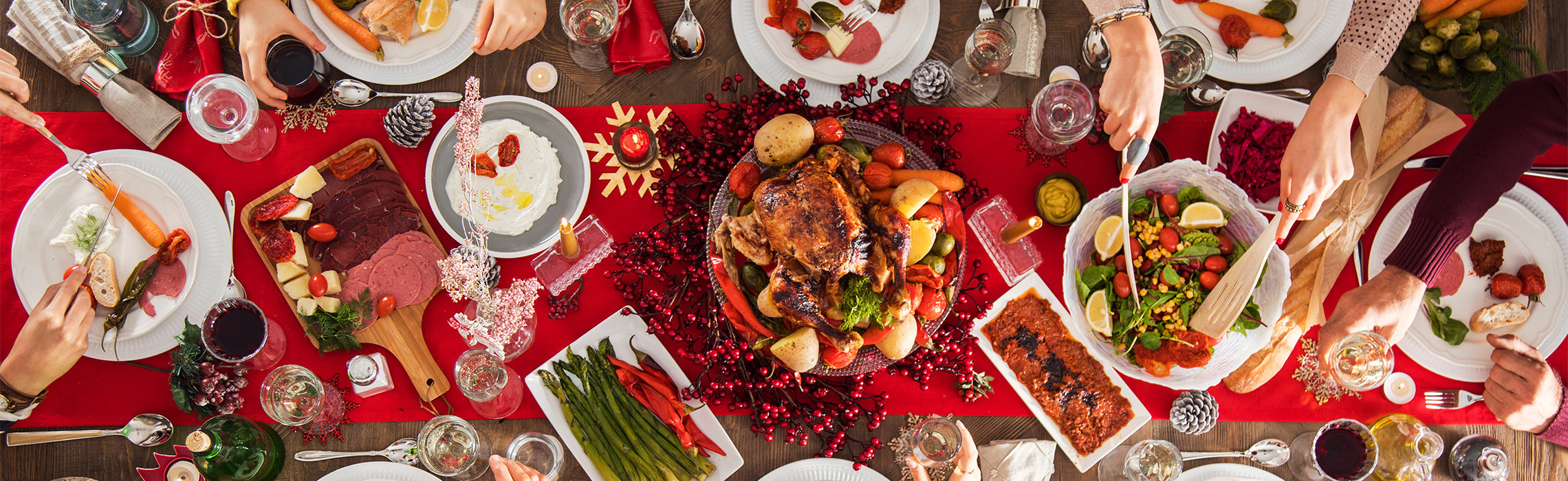 Overhead view of a festive holiday dinner table with roasted turkey, salads, side dishes, candles, and seasonal décor.