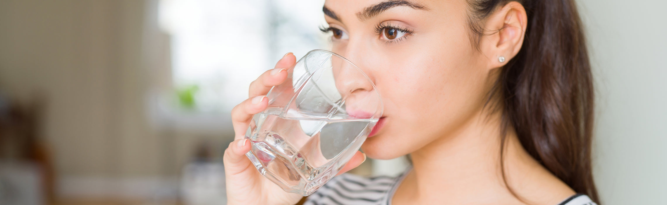 Close-up of a person drinking water from a clear glass indoors, representing hydration, healthy habits, and daily wellness.
