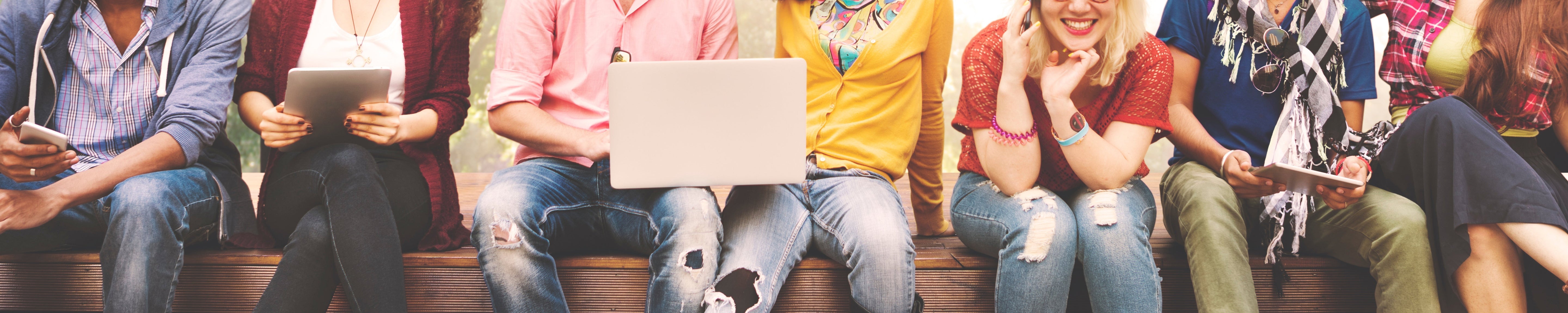 Group of people sitting side by side on a bench using smartphones, tablets, and a laptop, representing digital communication, technology use, social media, and connected lifestyles.