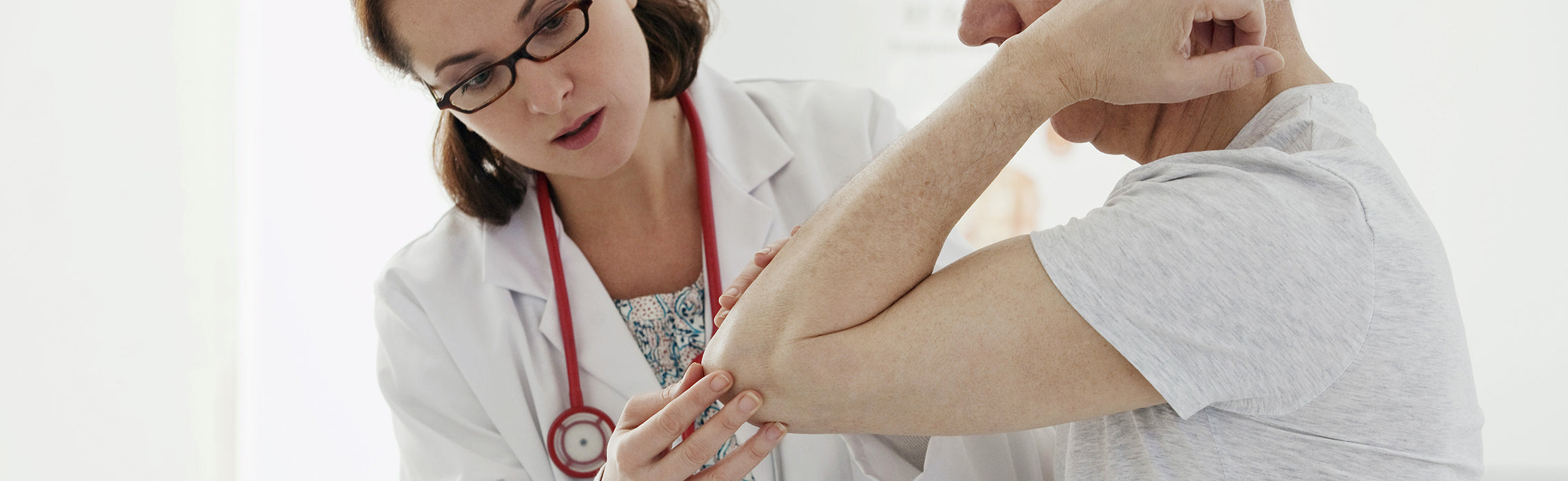 Healthcare provider wearing a lab coat and stethoscope examining a patient’s bent arm while holding the elbow joint, representing elbow pain, joint assessment, injury evaluation, and medical consultation for arm strain or tennis elbow.