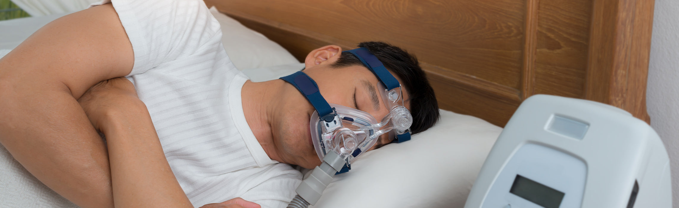 Person lying on a bed wearing a CPAP mask connected to a machine, resting on a pillow, representing sleep apnea treatment, breathing support, and improved nighttime sleep health.