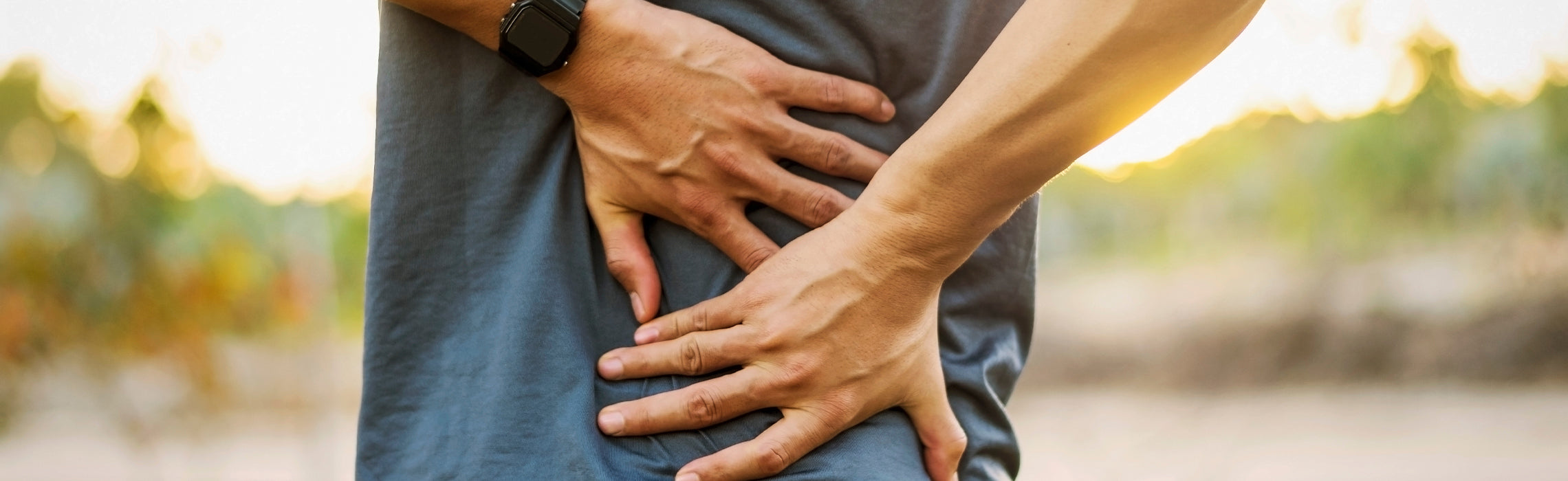 Person outdoors holding their lower back in pain with both hands