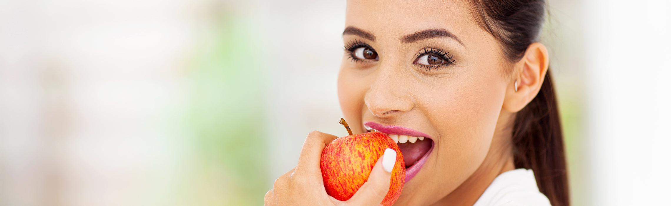 Close-up of a person eating a red apple, representing healthy eating, nutrition, and fresh fruit in a bright indoor setting.