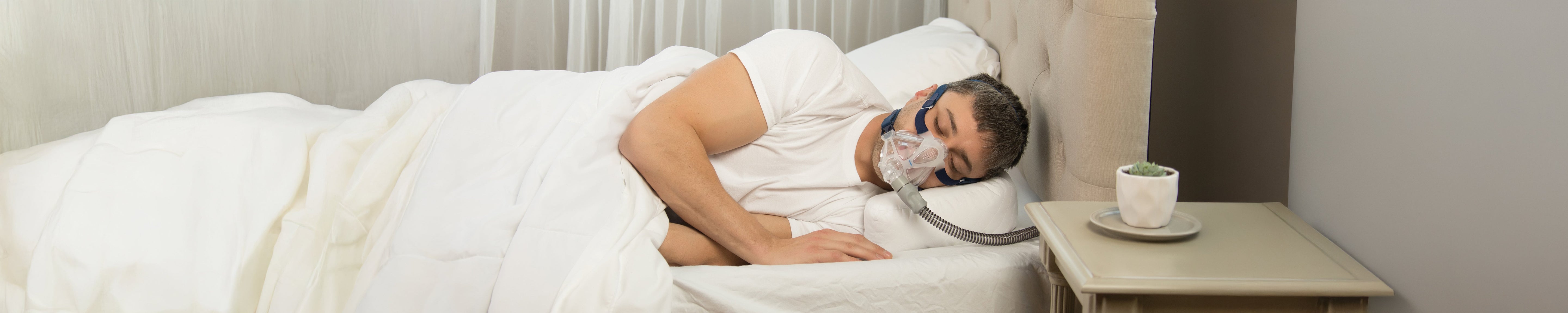 Man sleeping comfortably on her side in bed while wearing a CPAP mask for sleep apnea therapy.
