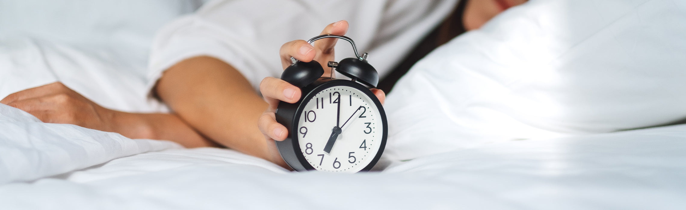 Person reaching to turn off an alarm clock while lying in bed