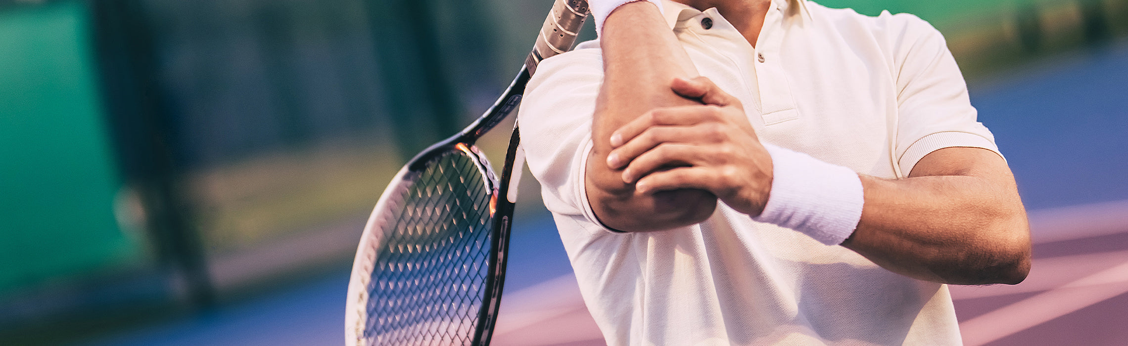 Person holding and gripping the forearm near the elbow with a tennis racket nearby, representing elbow pain, tennis injury, and sports-related joint strain during physical activity.