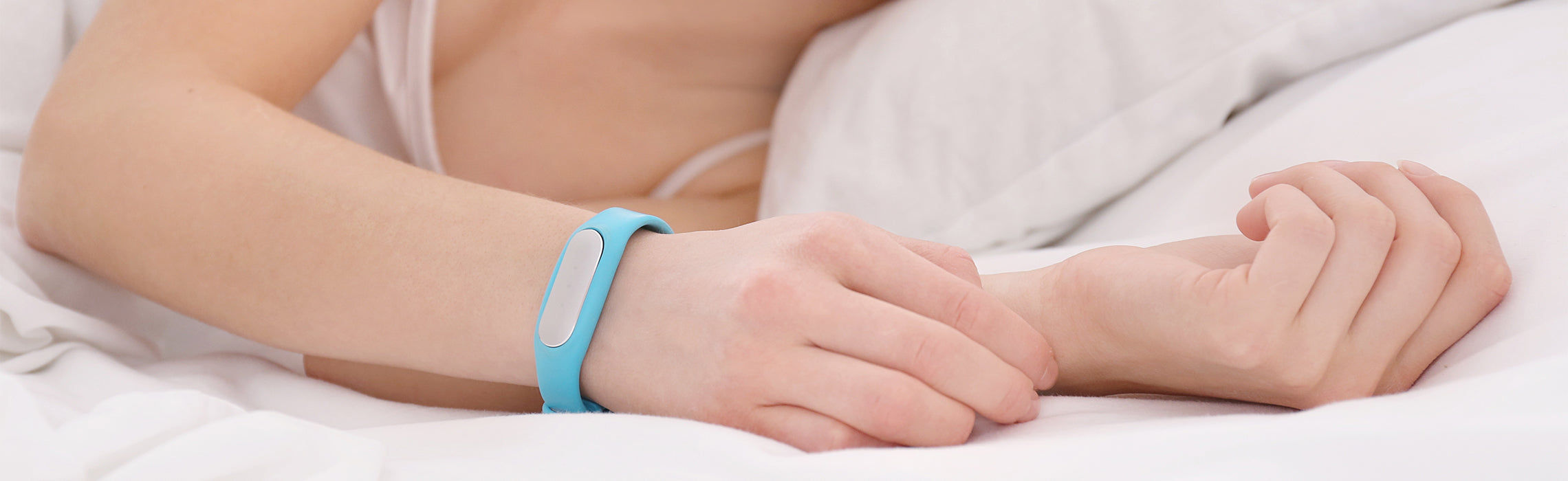 Close-up of a person lying in bed wearing a blue fitness tracker while holding the wrist, representing sleep monitoring, wrist pain, and wearable health technology in a restful setting.