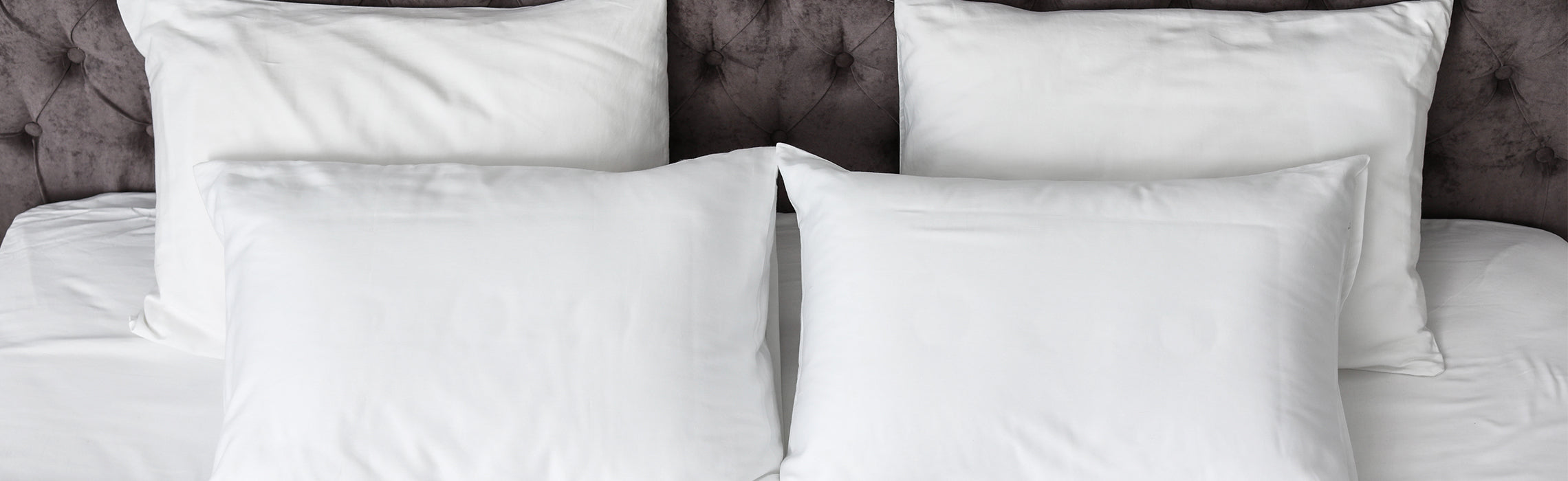 Neatly arranged white bed pillows displayed against a tufted upholstered headboard in a modern bedroom setting.