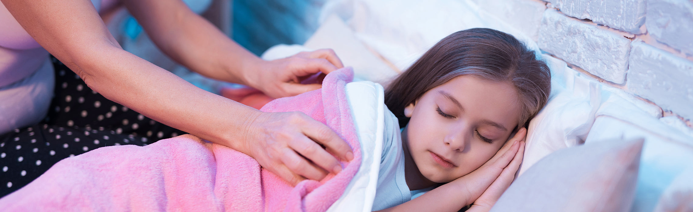 Child sleeping peacefully in bed with head resting on a white pillow while an adult gently tucks a pink blanket around the child, representing bedtime care, comfort, and restful sleep.