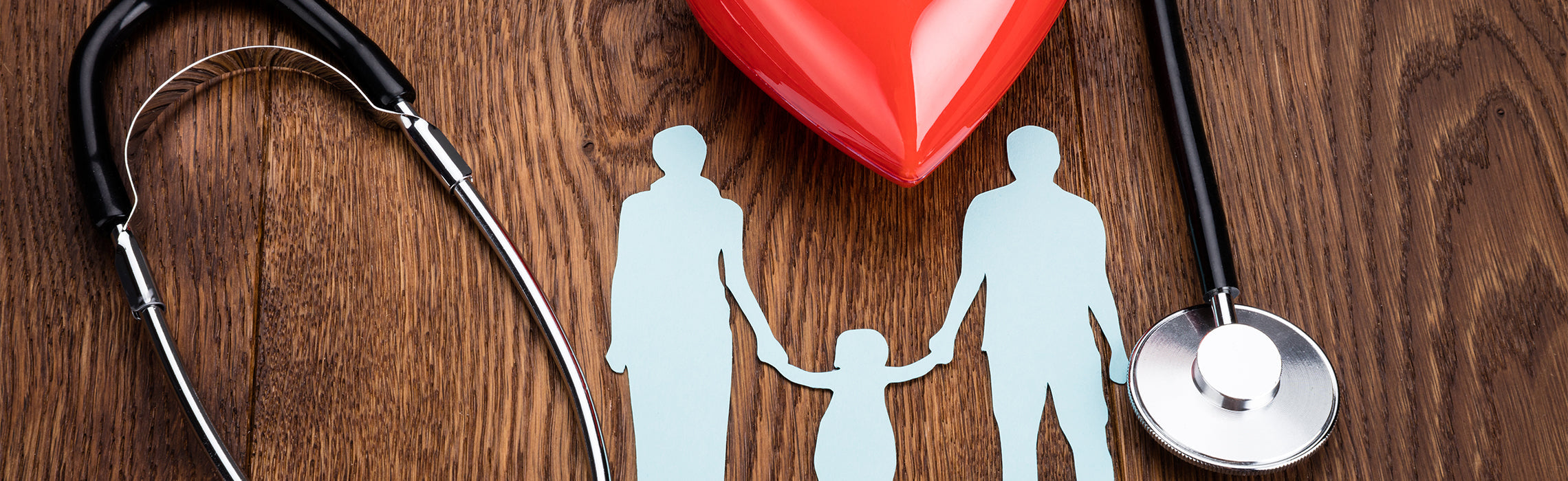 Flat lay of a red heart, stethoscope, and paper cutout family figures on a wooden surface, representing family health, healthcare protection, and preventive medical care.