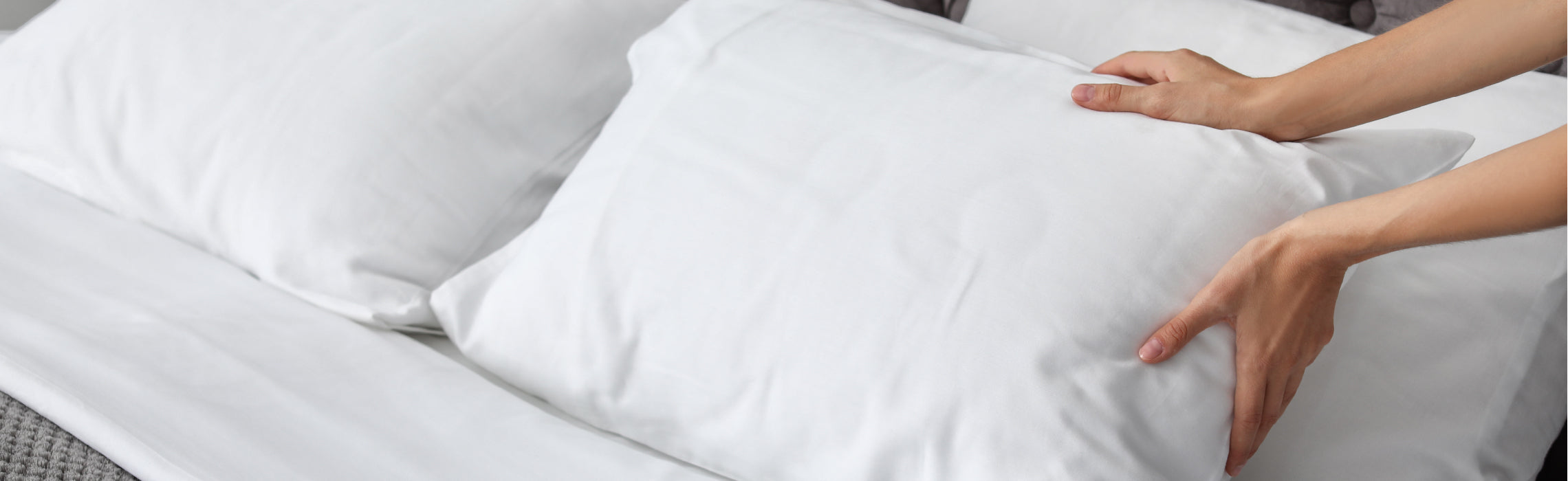 Hands placing and adjusting a white pillow on a neatly made bed with white sheets, representing bedding setup, sleep comfort, and proper pillow support for restful sleep.