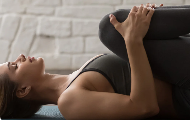 Person performing a knee-to-chest stretch on a yoga mat indoors to improve flexibility and support knee health.
