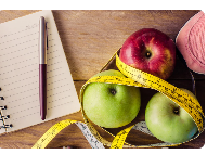 Flat lay with apples wrapped in a measuring tape, notebook, running shoe, and water bottle, representing healthy eating, fitness planning, and wellness goals.