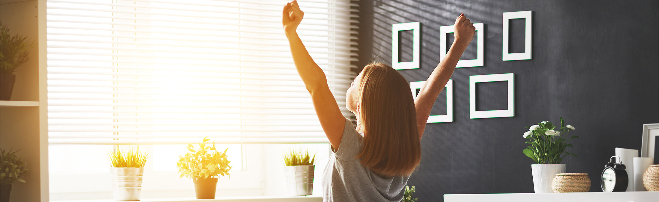 Alt text: Woman stretching her arms in a bright bedroom after waking up, symbolizing restful sleep, morning wellness, and healthy daily routines.