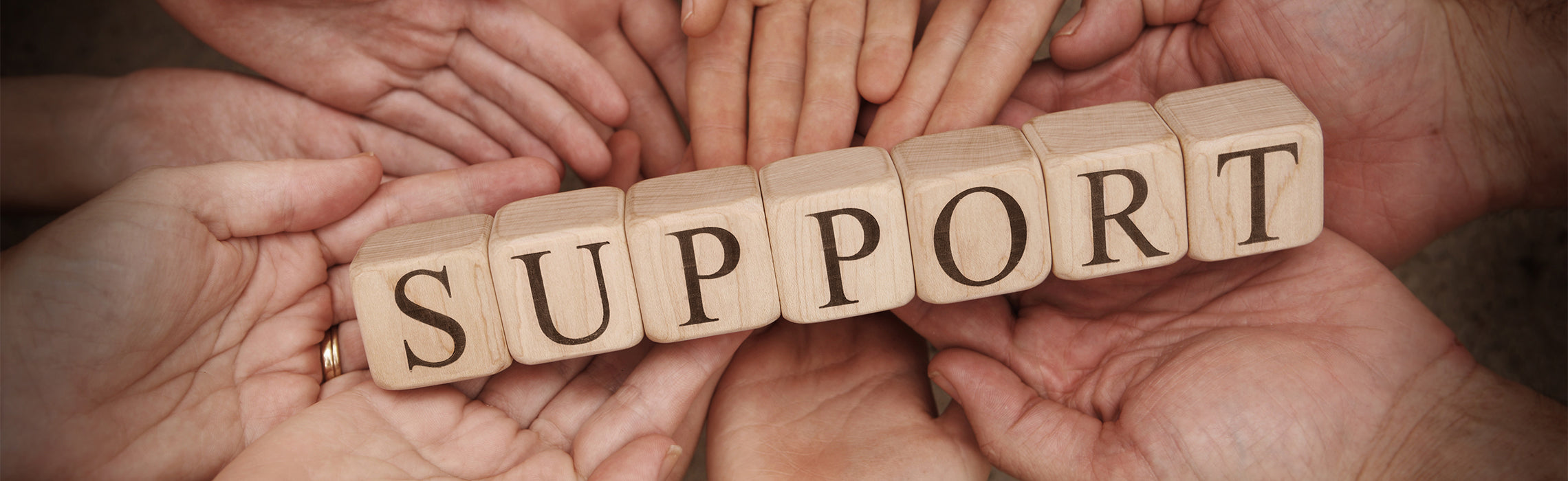 Hands holding wooden blocks spelling “SUPPORT,” symbolizing teamwork, community, assistance, and helping others. Visible text: “SUPPORT.”