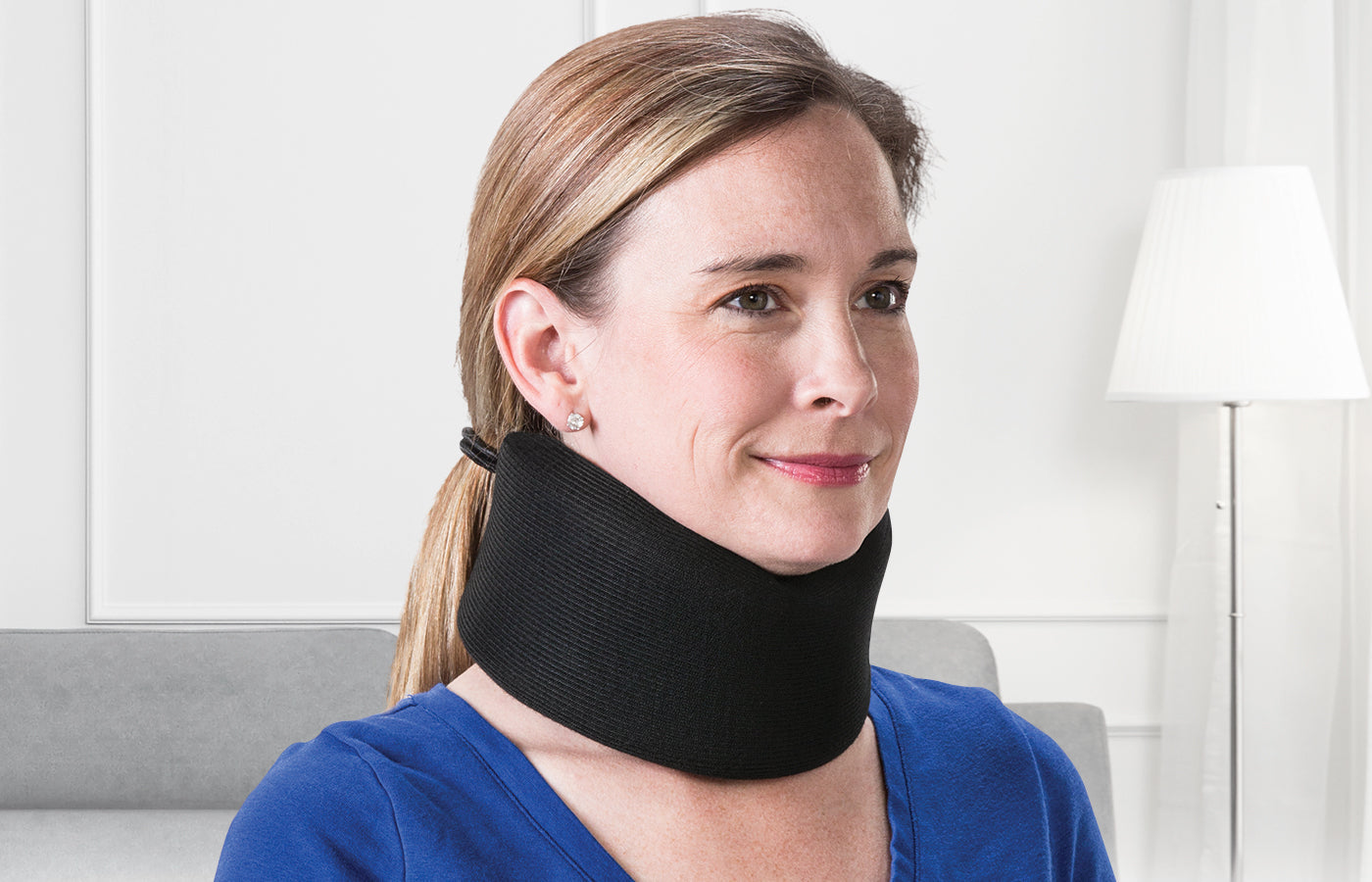 Close-up of a person wearing a black cervical neck support collar while seated indoors, representing neck pain relief, posture support, and injury recovery.