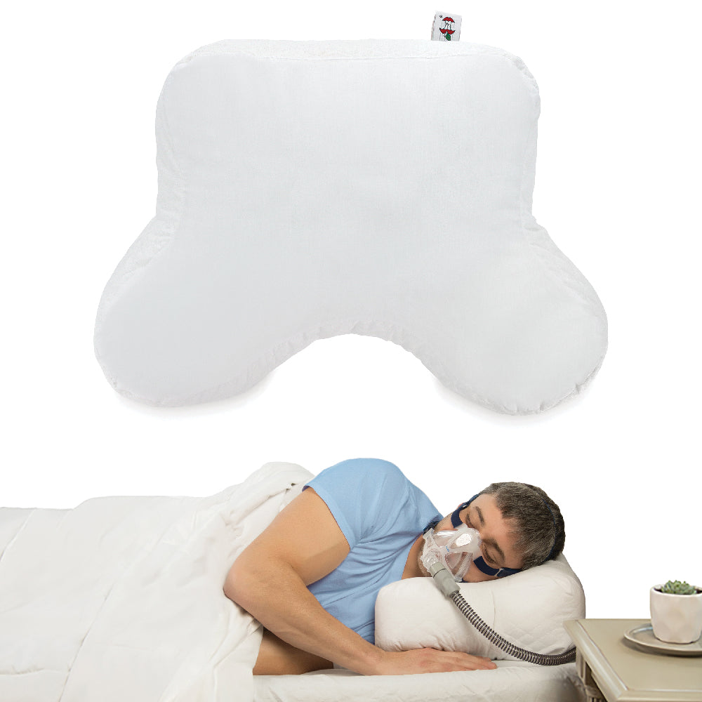Core Products® CPAP Pillow featuring a white contoured design with curved shoulder cutout and side extensions for comfortable sleep positioning. The image shows the pillow above a man sleeping on his side while wearing a CPAP mask, with the hose extending over the pillow's edge. The specially shaped pillow helps provide mask and hose clearance, reduce pressure points, and support more comfortable side sleeping during CPAP therapy.