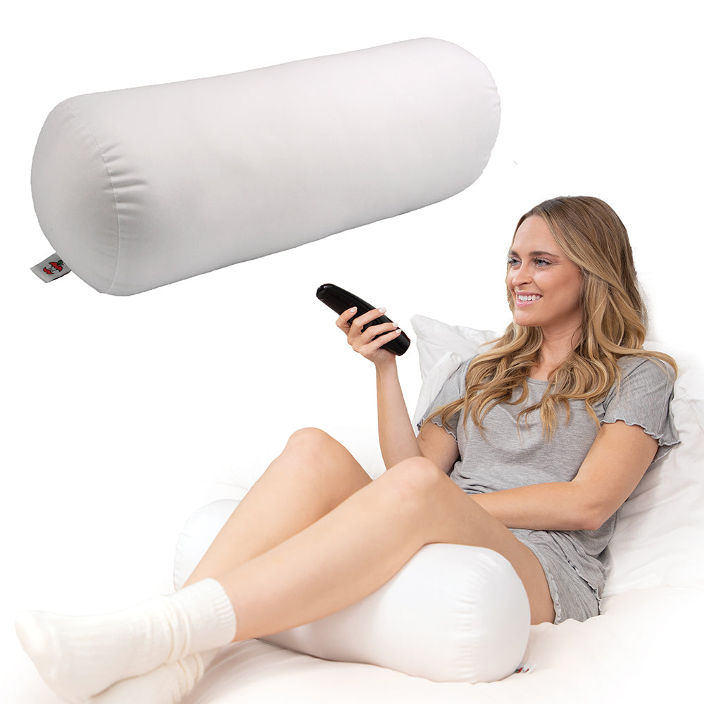 Core Products Jackson Roll Positioning Support Pillow in white shown supporting a woman sitting comfortably in bed. Cylindrical fiber-filled pillow provides versatile support for legs, knees, and back, promoting proper alignment, relaxation, and everyday comfort.